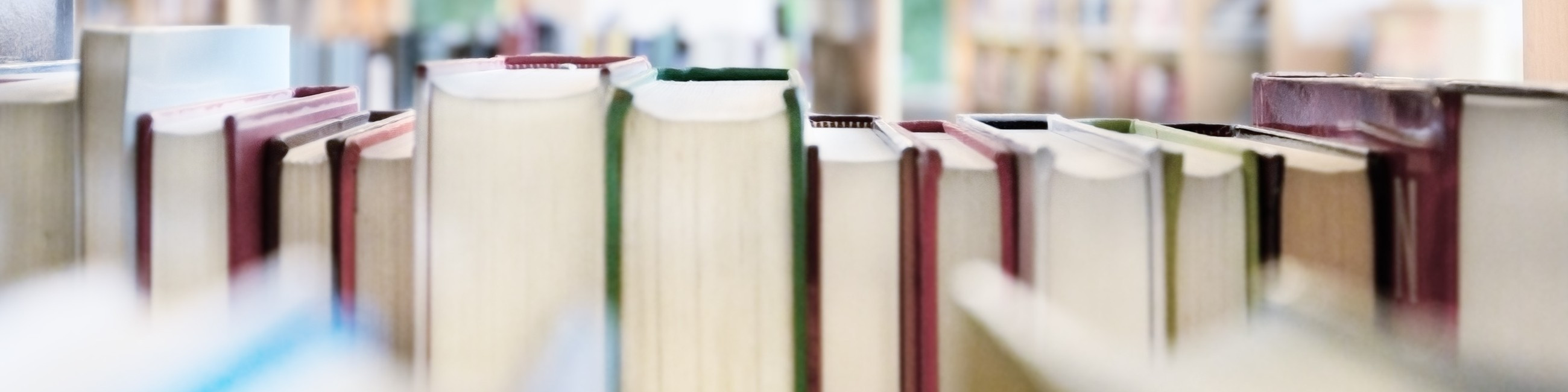Close-up of book spines on a library shelf, with colorful bindings in focus against a blurred background.