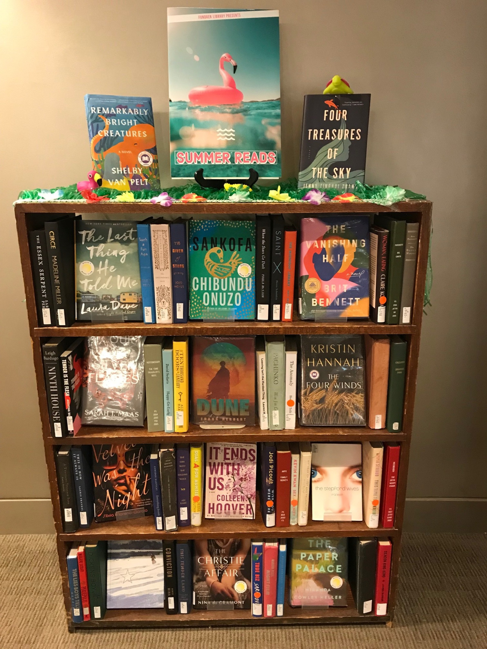 Book display with summer reads, some facing out and some spine-out on the bookcase, and a pink flamingo poster on top of the shelf